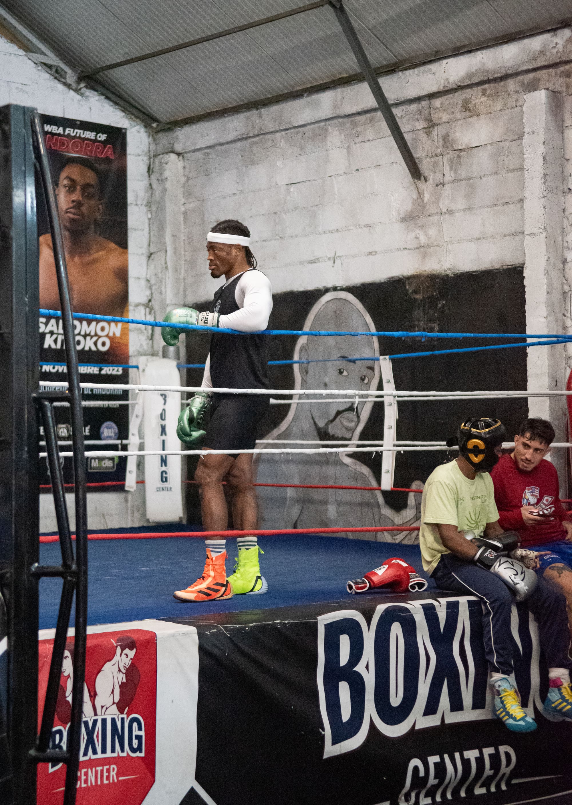 Un boxeur s'entraîne dans le ring pendant que d'autres pratiquants observent depuis le bord.