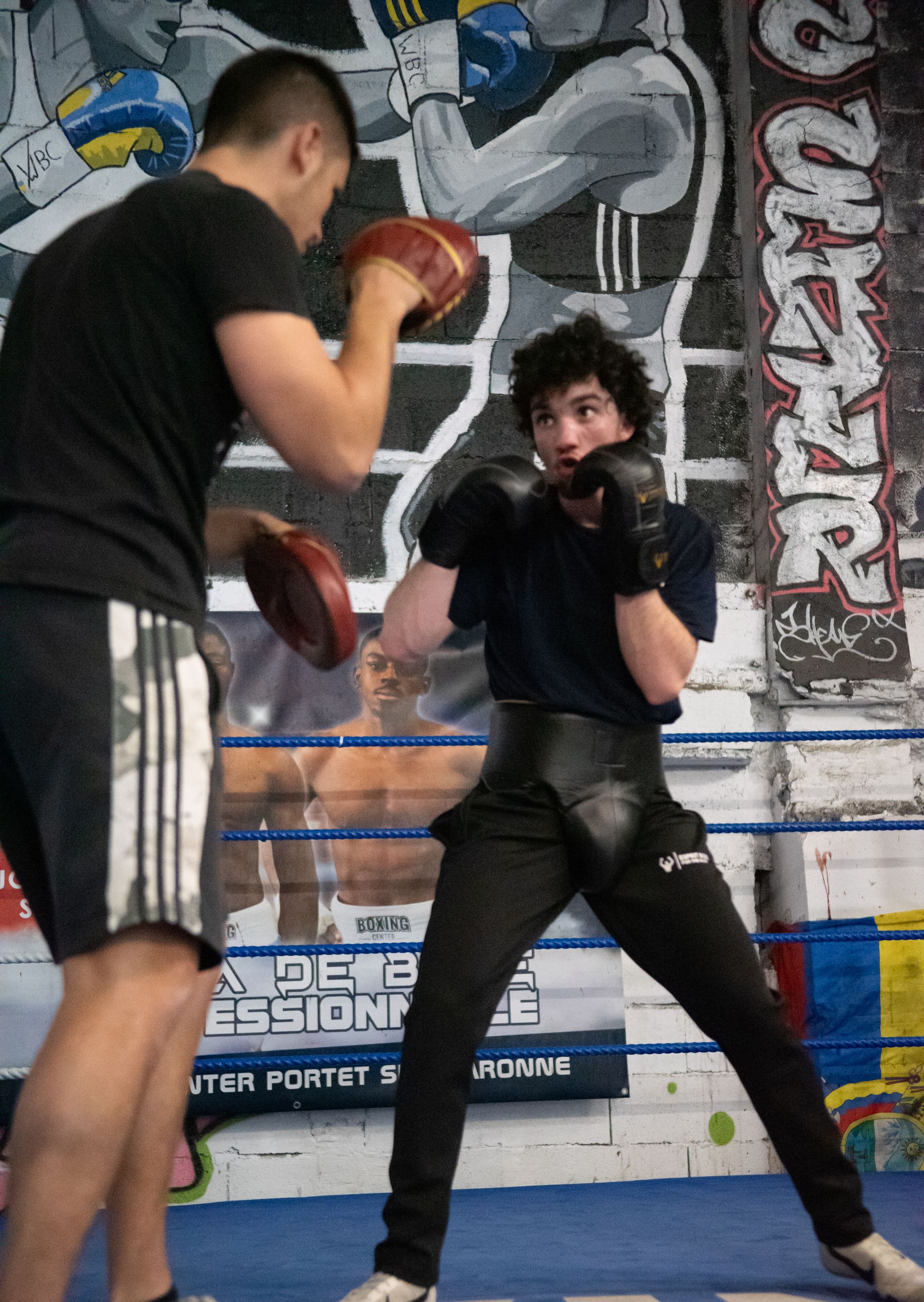Un boxeur en garde face à un coach qui tient les pattes d'ours, dans le ring.