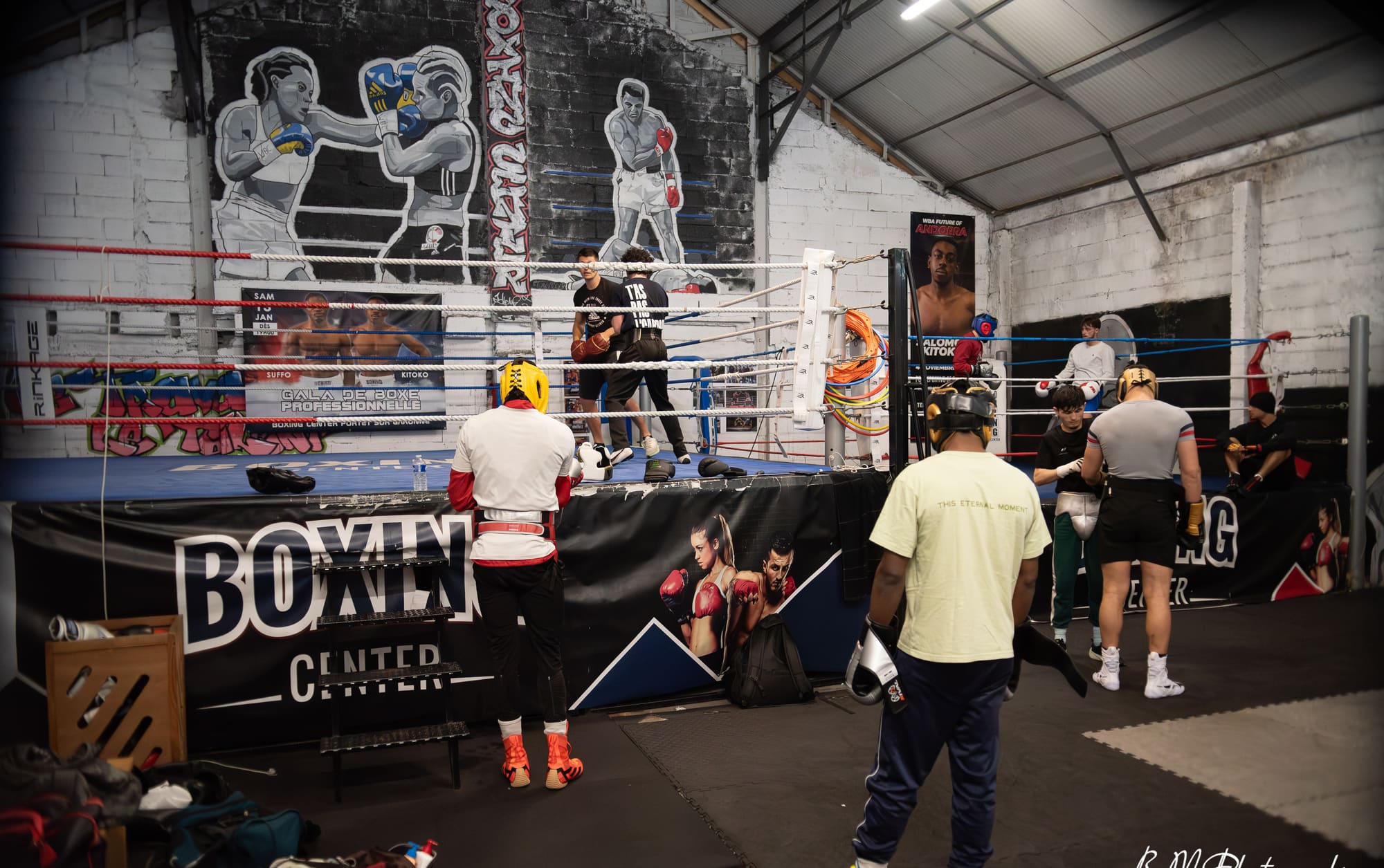 Vue large de la salle pendant un cours collectif : plusieurs pratiquants autour et sur le ring.
