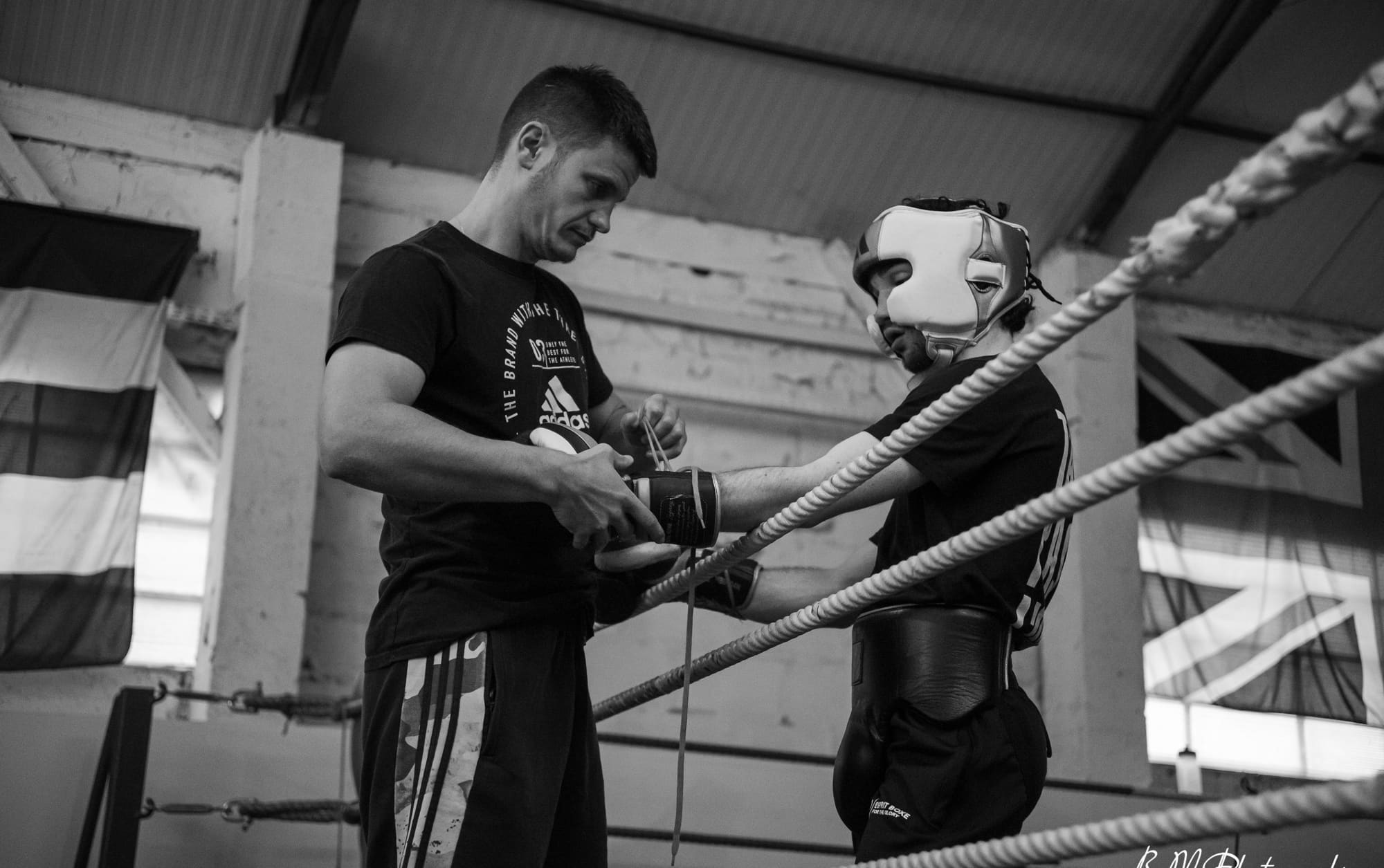 Un coach ajuste les gants d'un boxeur casqué avant de monter sur le ring.