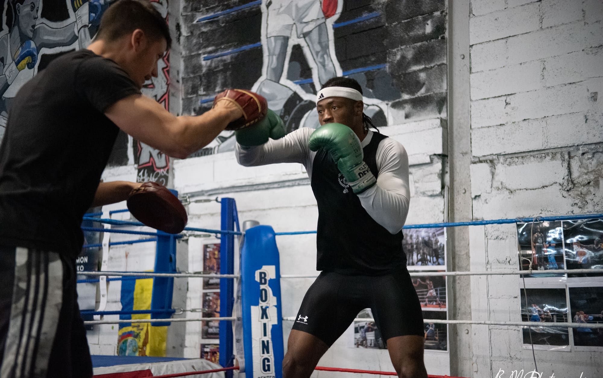 Un pratiquant enchaîne des frappes sur les pattes d'ours tenues par un coach, dans le ring.
